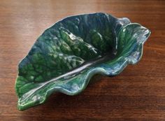 a green leaf shaped bowl sitting on top of a wooden table