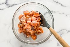 a glass bowl filled with diced carrots next to a wooden spoon on top of a marble counter