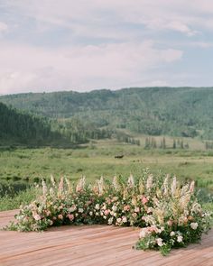 an outdoor ceremony setup with flowers and greenery on a wooden deck in the mountains