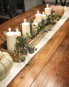 candles are lit on a long table with white pumpkins and greenery