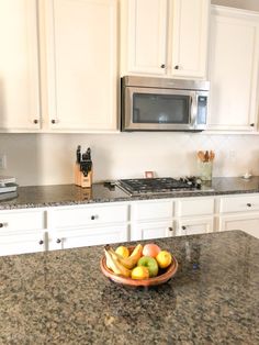 a bowl of fruit sitting on top of a kitchen counter next to a microwave oven