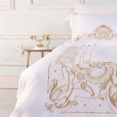 a bed with white and gold comforters on top of it in a room next to a wall