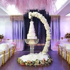 a white wedding cake on top of a table in front of purple draping