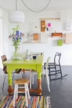 a green table and chairs in a white room with colorful rugs on the floor