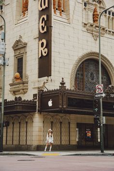 a woman walking across the street in front of an old theater