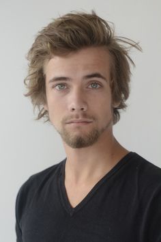 a man with long hair and beard wearing a v - neck shirt looking at the camera