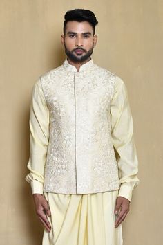 Cream sleeveless bundi with thread embroidery in floral pattern and mandarin collared neckline. Paired with full sleeve draped kurta and white churidar. - Aza Fashions Luxury Chanderi Nehru Jacket With Mandarin Collar, Luxury Long Sleeve Chanderi Nehru Jacket, Luxury Cotton Silk Nehru Jacket With Cutdana, Luxury Silk Nehru Jacket With Traditional Drape, Luxury Raw Silk Nehru Jacket With Traditional Drape, Luxury Cotton Nehru Jacket With Traditional Drape, Luxury Cream Raw Silk Nehru Jacket, Luxury White Cotton Silk Nehru Jacket, White Churidar