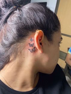 a woman with a butterfly tattoo on her left side behind the ear is looking at another person