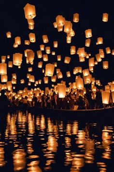 a boat filled with lots of paper lanterns floating in the air over water at night