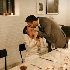 a man kissing a woman at a dinner table with candles on the table and chairs around it