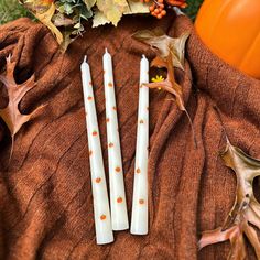 three white candles sitting on top of a brown cloth next to leaves and pumpkins