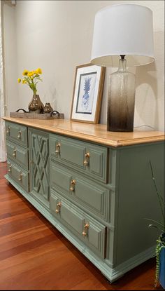 a green dresser with two pictures on top and a lamp in the corner next to it