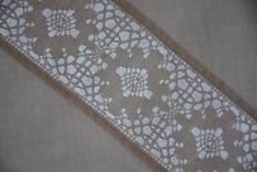 a white lace with flowers on it is laying on a table cloth that has been cut in half