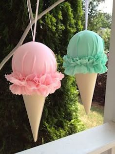 two ice cream cones hanging from a window sill with pink and blue frosting on them