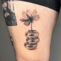 a black and white photo of a flower in a vase on the side of a man's thigh