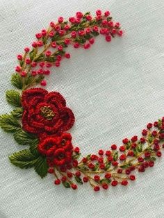 red flowers and green leaves are arranged on a white table cloth with embroidery work in the middle