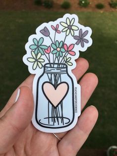 a hand holding a sticker with flowers in a mason jar