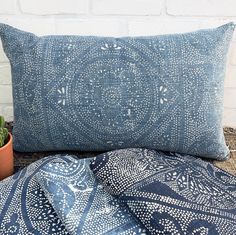 a blue and white pillow sitting on top of a bed next to a potted plant