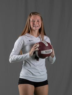 a woman holding a football in her right hand and posing for a photo with the ball