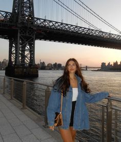 a woman standing on the side of a bridge next to a body of water with a large bridge in the background