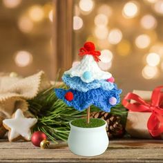 a crocheted christmas tree in a white pot on a wooden table next to presents