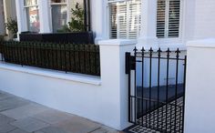 a white house with black iron fence and window boxes on the front door, next to a brick sidewalk