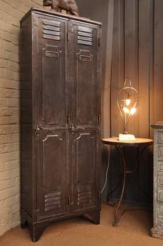 an old metal locker next to a table with a lamp on it and a cat statue on top