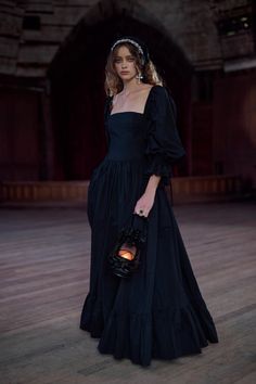 a woman in a long black dress holding a lantern and wearing a headpiece with her hair pulled back