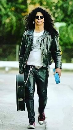 a man walking down the street with a suitcase and water bottle in his hand while wearing black leather pants