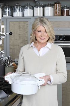 a woman is holding a pot in her hands and smiling at the camera while standing in front of an oven