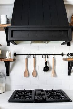 a stove top oven sitting under a black hood over an oven with utensils hanging from it