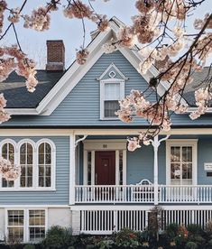 a blue and white house with cherry blossoms on the front porch in blooming trees