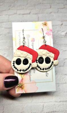 a pair of skully earrings with santa hats on them are being held up by someone's hand