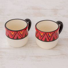 two coffee mugs sitting on top of a white table next to each other,