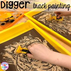 a child's hands are painting with construction trucks on paper and yellow trays