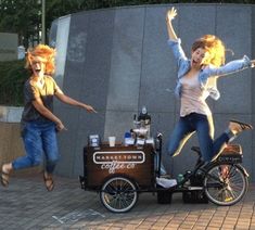 three people are jumping in the air near a coffee cart and bike with an ice cream vendor on it