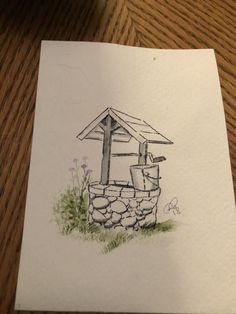 a drawing of a small house made out of rocks on a wooden table next to a pen and paper