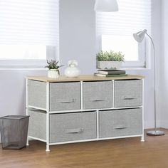 a white dresser with four drawers in front of a window and a gray trash can