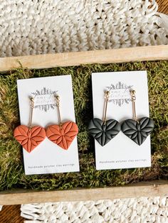 two earrings with black and orange hearts on them in a wooden box next to some grass