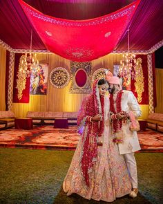 the bride and groom are posing for a photo in front of an elaborate stage with red drapes