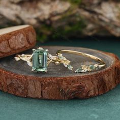 an emerald colored ring sitting on top of a piece of wood with other jewelry items around it