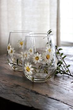 three wine glasses with daisies painted on them sitting on a table next to a window