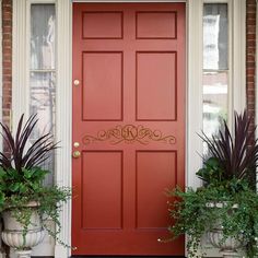 a red door with welcome written on it and two potted plants next to it