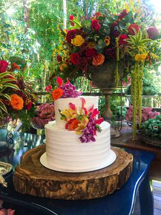 there is a white cake with flowers on the table next to other flowers and greenery