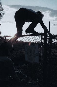 a skateboarder is doing a trick on a chain link fence as the sun sets