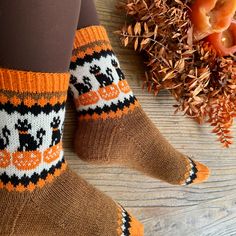 the legs of a woman wearing brown socks with black and white cats on them next to dried flowers