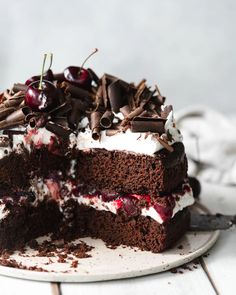 a piece of chocolate cake with cherries and whipped cream frosting on a white plate