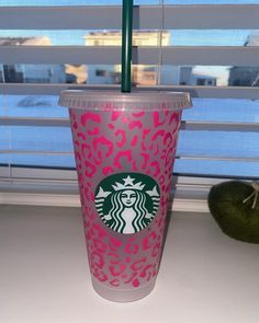 a starbucks cup sitting on top of a counter next to a green apple in front of a window