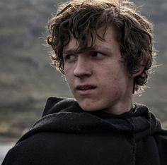 a young man with curly hair wearing a black hoodie and looking at the camera