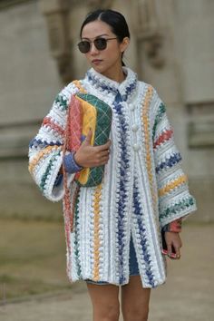 a woman is walking down the street wearing a crocheted coat and holding a purse